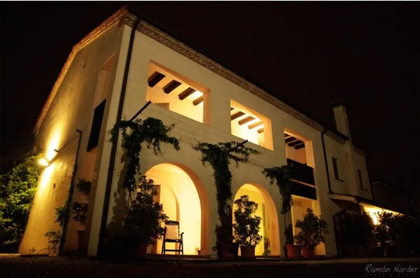 Experience the charm of a classic building with a symmetrical facade and arched doorways, set amidst lush greenery.