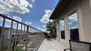 A balcony with a view of a parking lot and buildings, a patio area with chairs, and a large window. - The Blue Llama- on the Guadelupe river! 2 pools, 1 heated, 4 hot tubs (New Braunfels)