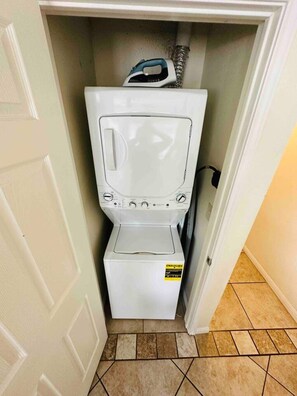 A compact, white laundry machine in a small, enclosed space with tiled flooring.