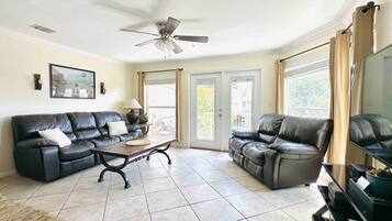 A living room with two black leather sofas, a coffee table, a ceiling fan, and a television.