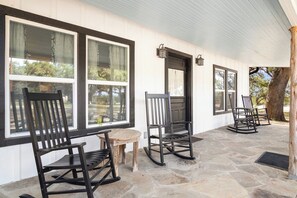 A covered porch with stone flooring, black rocking chairs, and a wooden table.