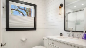 Casa de banho com sanita, lavatório com espelho e janela com estores.