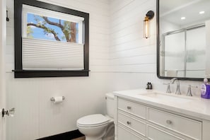 Ein Badezimmer mit Toilette, Waschbecken mit Spiegel und einem Fenster mit Jalousien.