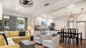 Uma sala de estar ampla, com sofá, poltronas, mesa de centro e área de jantar com mesa e cadeiras.