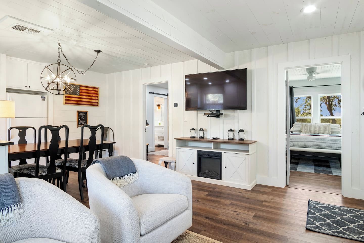 A spacious living room with a dining area, a flat-screen TV mounted on the wall, and a cozy seating area with armchairs.