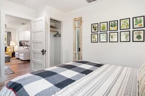 A bedroom with a checkered bedspread, a wardrobe, and a wall with botanical prints. - Hill Country Mirage | 3BR Farmhouse w/ Pond & Bar (Bandera)