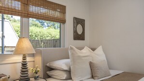 A bedroom with a bed, pillows, a bedside table with a lamp, and a window with a view of greenery. - Downtown Sebastopol Studio (Sebastopol)
