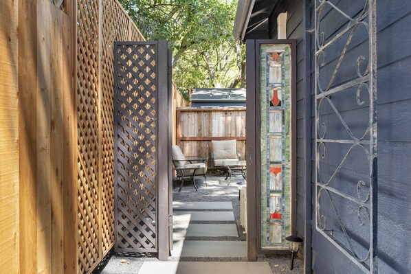 A wooden fence with a lattice design, a glass door with a decorative frame, and a view of a patio area with outdoor furniture. - Downtown Sebastopol Studio (Sebastopol)