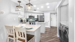 A modern kitchen with white cabinets, a central island, and stainless steel appliances. There are two pendant lights above the island.