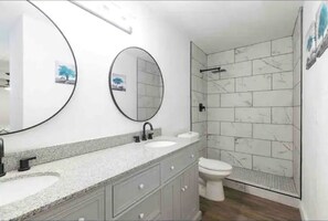 A modern bathroom with a vanity, two sinks, a toilet, and a shower area with marble tiles. - Family Oasis 10 min from Fiesta Tx (San Antonio)
