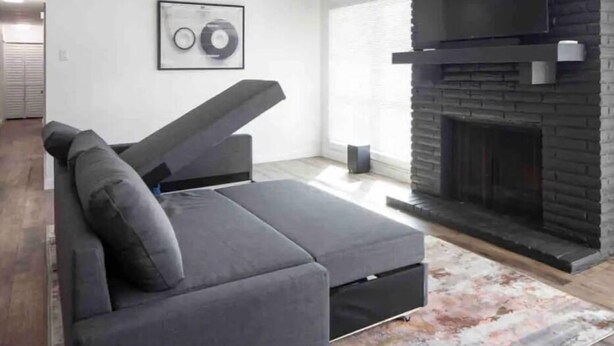 Ein modernes Wohnzimmer mit einem grauen Ecksofa, einem Kamin und einem gerahmten Bild an der Wand.
