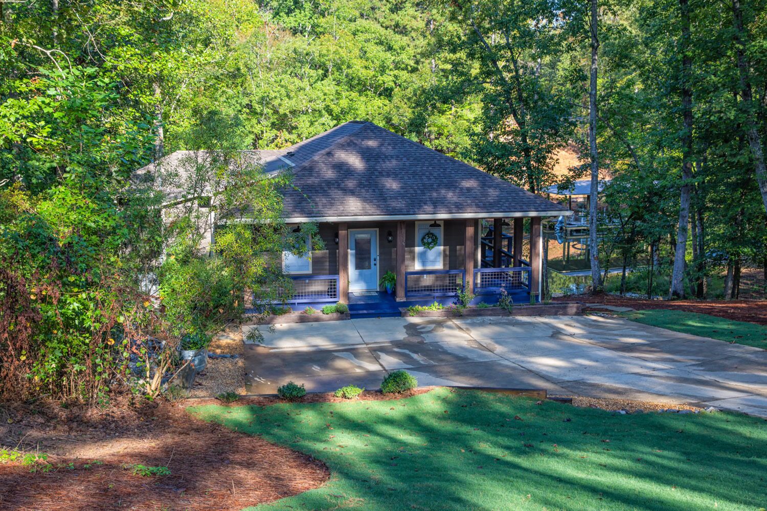 A single-story house with a covered porch, surrounded by dense trees and a well-maintained lawn.