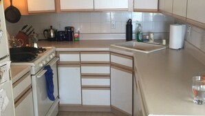 Una cocina compacta con armarios blancos, estufa, lavamanos y ventilador de techo.