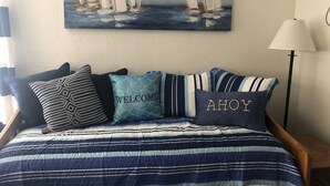 Una cama con una colcha azul y blanca a rayas, almohadas con texto y un cuadro de barcos de vela en la pared.