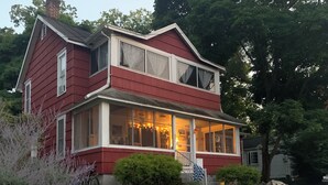 A two-story house with a large front porch, a staircase leading to the entrance, and a well-maintained garden with a lawn and shrubs. - Spacious 5 Bedroom House On Double Lot In Lakeside One Block From The Lake! (Lakeside Marblehead)