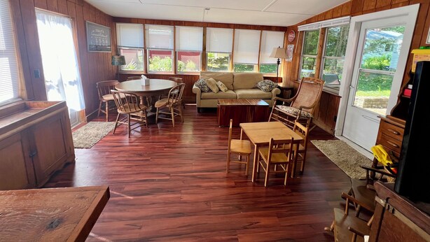A spacious living room with a wooden floor, a round dining table, a sofa, and a ceiling fan. - Spacious 5 Bedroom House On Double Lot In Lakeside One Block From The Lake! (Lakeside Marblehead)