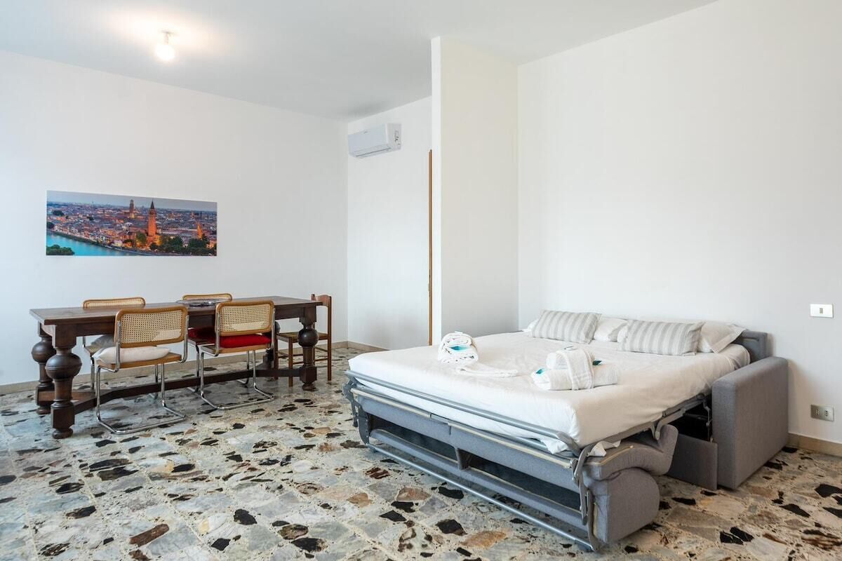Una habitación compacta con una cama, una mesa de comedor con sillas y un cuadro de un paisaje urbano en la pared.