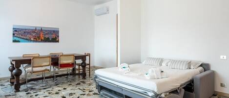 Una habitación compacta con una cama, una mesa de comedor con sillas y un cuadro de un paisaje urbano en la pared.