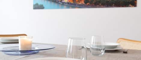 A dining table with plates, glasses, and a candle, set against a wall with a cityscape painting.