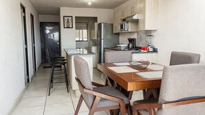Una cocina compacta con comedor, que incluye una mesa de madera, sillas tapizadas en gris y electrodomésticos modernos.