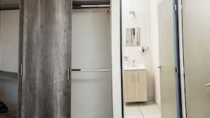Un dormitorio con cama, un pilar de madera, ventilador de techo y vistas hacia un baño con lavamanos y espejo.