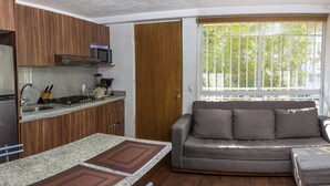 Une cuisine compacte équipée d’un réfrigérateur, d’un four à micro-ondes et d’une cuisinière, d’un meuble en bois et d’une fenêtre donnant sur les arbres.