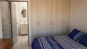 A bedroom with a bed, a wardrobe, a mirror, and a bathroom with a sink.