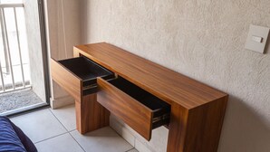 A wooden desk with two drawers against a textured wall, a window with a metal gate, and a tiled floor.