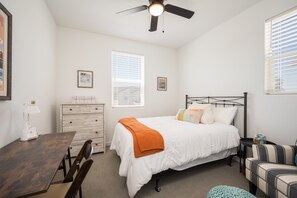 Ein Schlafzimmer mit Bett, Schreibtisch, Stuhl, Kommode und Deckenventilator.