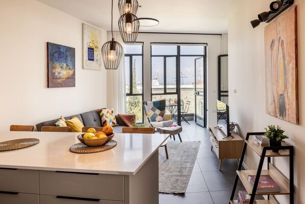 A modern kitchen with a central island, a dining area with a sofa, and a view through large windows.