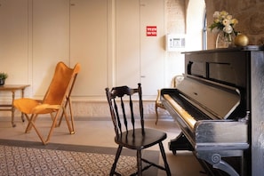 Un piano, une chaise en bois et une petite table dans une pièce dont le sol est recouvert d’un motif décoratif.