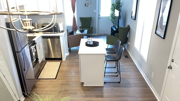 Eine moderne Küche mit Edelstahlgeräten, ein Essbereich mit Glastisch und Stühlen sowie ein Wohnzimmer mit Sofa und Couchtisch.