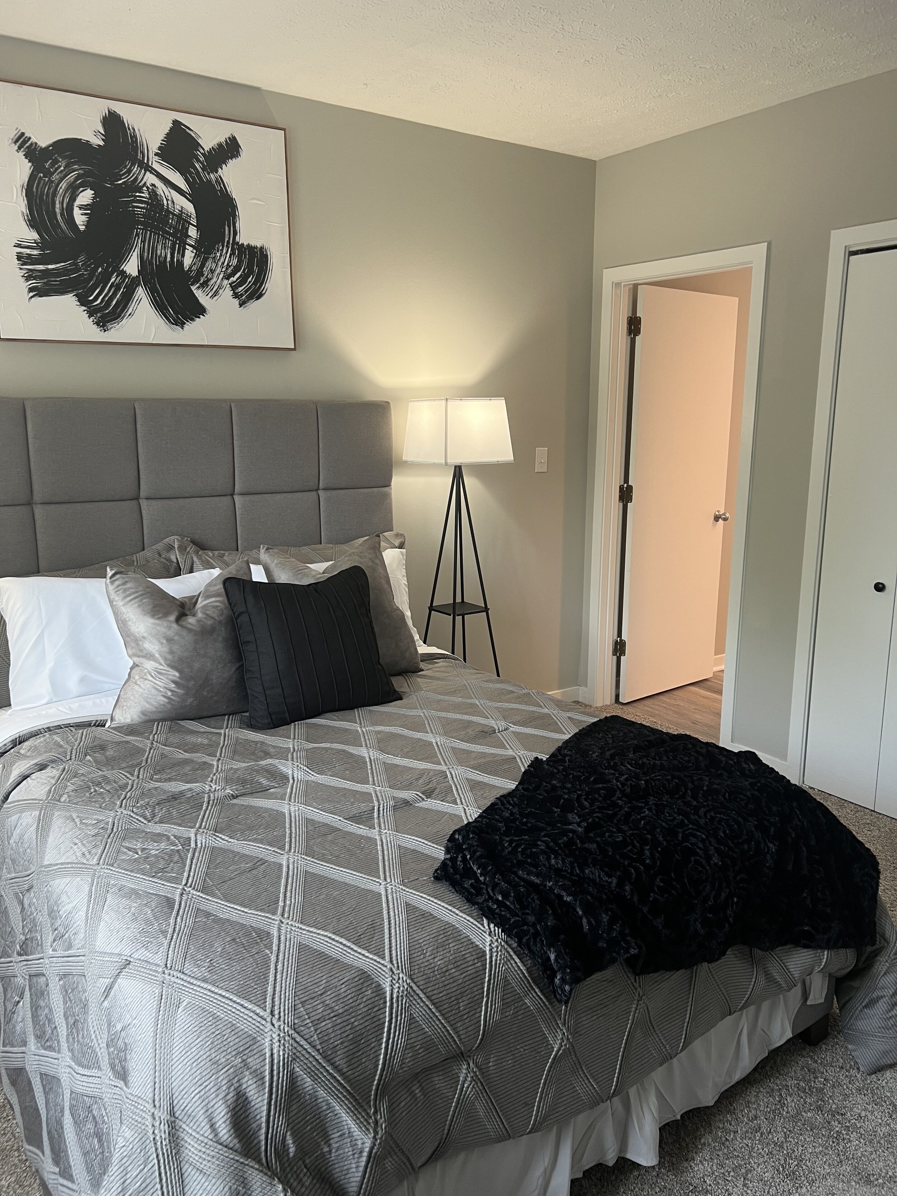 Une chambre avec un grand lit, une lampe sur pied et une porte donnant sur une autre pièce.