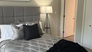 Une chambre avec un grand lit, une lampe sur pied et une porte donnant sur une autre pièce.
