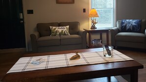 Un salon comprenant un canapé, une table basse, une lampe, une fenêtre avec des stores et une porte.
