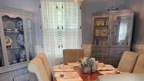 A dining room with a wooden table, four chairs, a chandelier, and a cabinet with glass doors.