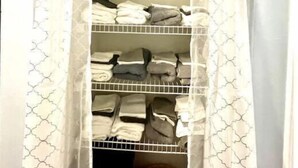 A closet with three shelves, each holding folded clothes.