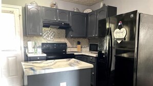 A kitchen with dark cabinets, a black refrigerator, a microwave, and a stove.