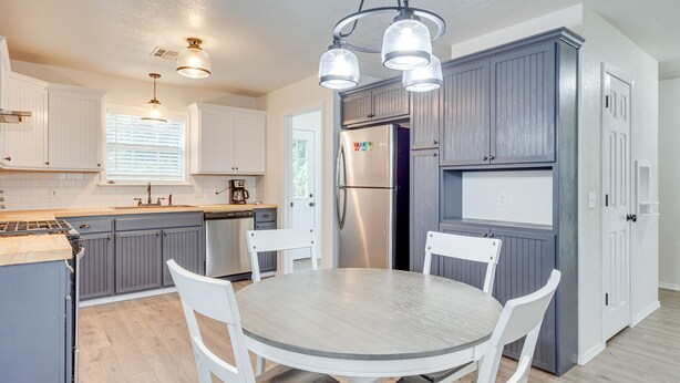 A modern kitchen with grey cabinets, a stainless steel refrigerator, white chairs, and a round table. - Updated Home w/ Yard ~ 14 Mi to Quartz Mountain! (Mangum)