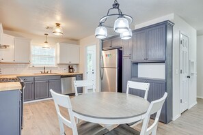 A modern kitchen with grey cabinets, a stainless steel refrigerator, white chairs, and a round table. - Updated Home w/ Yard ~ 14 Mi to Quartz Mountain! (Mangum)
