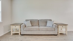 A neutral-toned living room with a beige sofa, two matching nightstands, and a window on the left. - Updated Home w/ Yard ~ 14 Mi to Quartz Mountain! (Mangum)