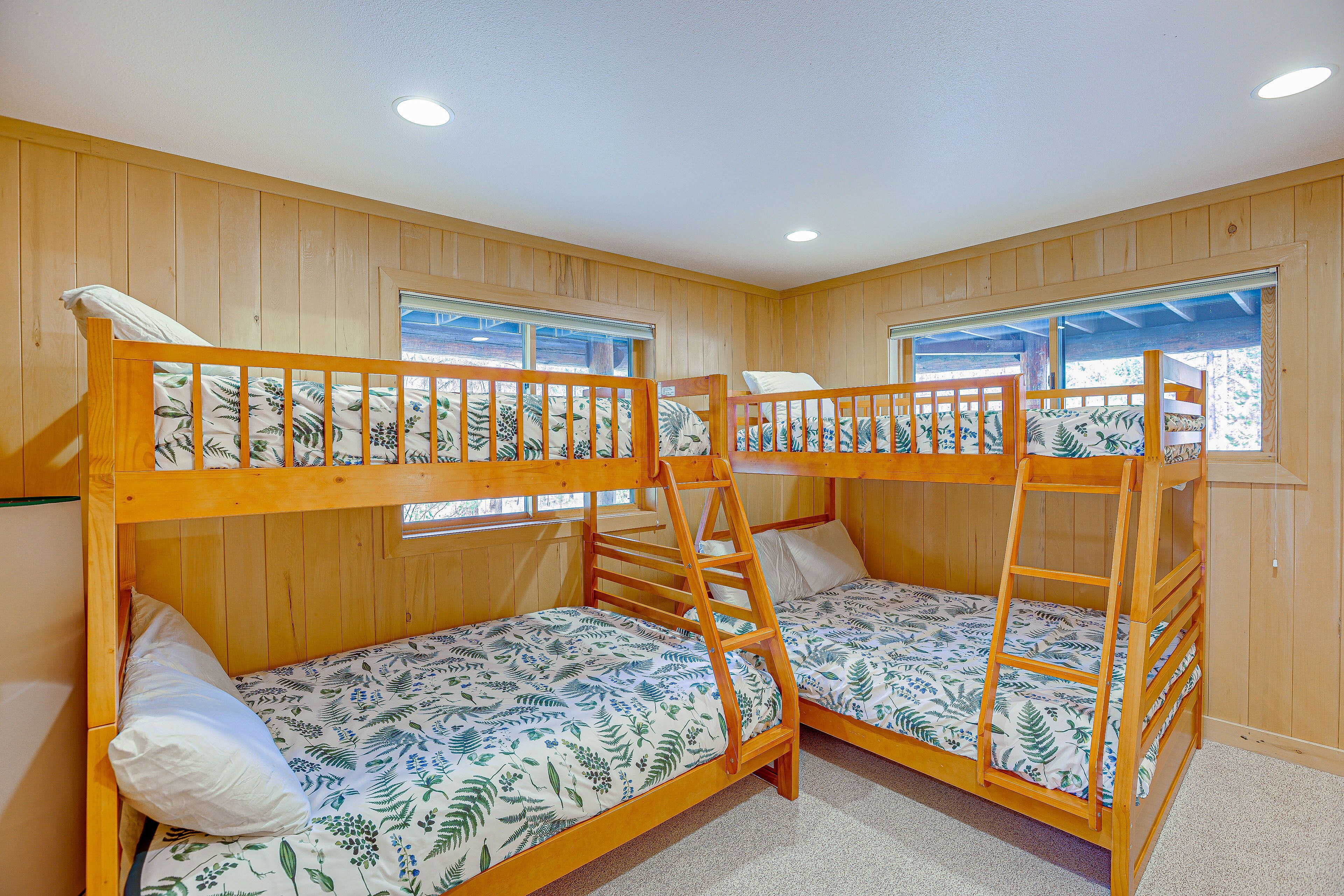 Quarto com duas beliches, paredes de madeira e janelas com persianas.
