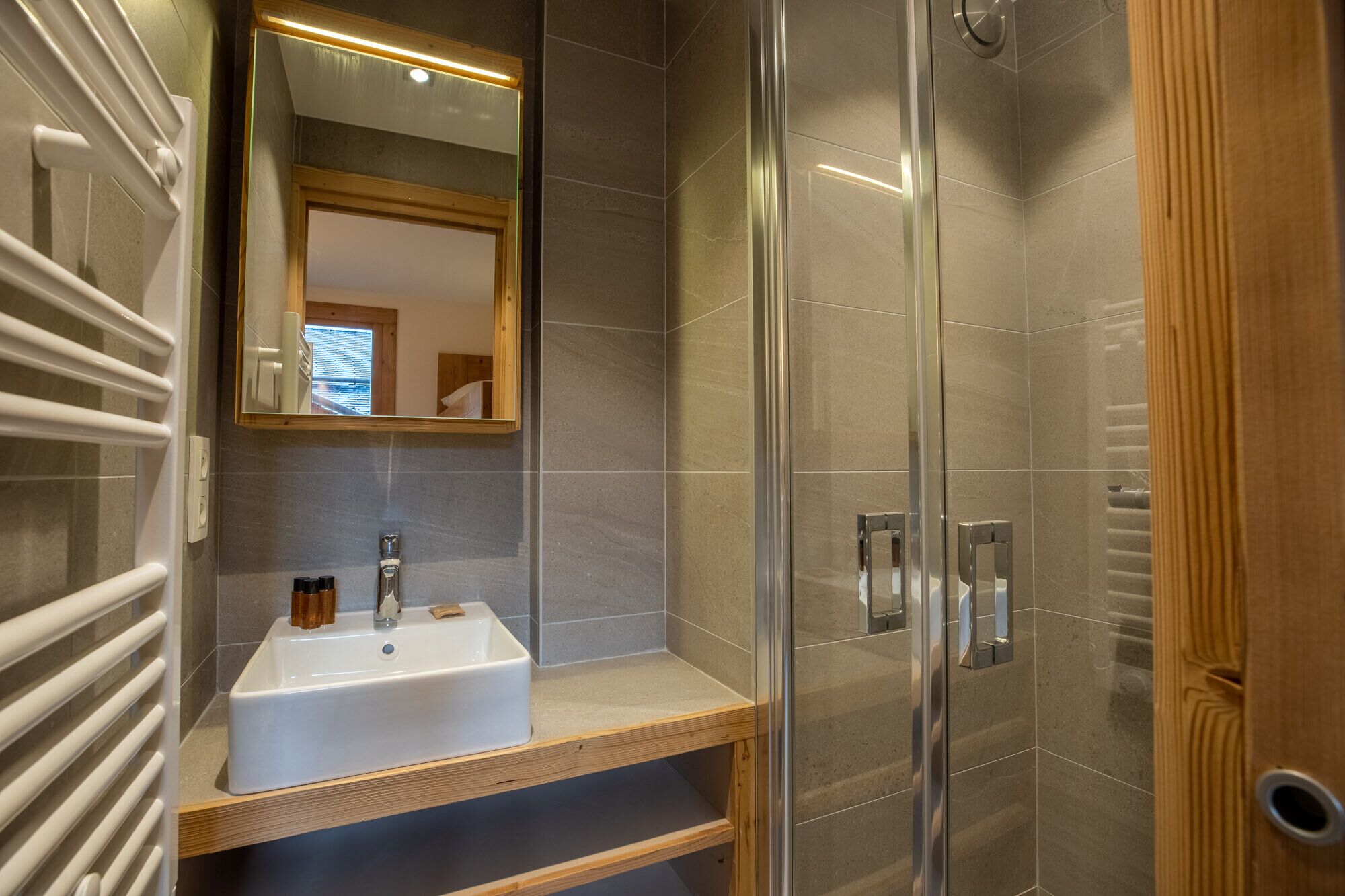 Een moderne badkamer met een douchecabine van glas, een wit wastafelmeubel met een houten blad en een spiegel met ingebouwde verlichting.