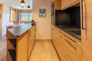 Uma cozinha moderna com armários de madeira, bancada preta e janela com vista para uma floresta.