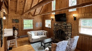 A wooden cabin interior with a stone fireplace, wooden floors, and a ceiling fan. - Hillside Haven - peaceful, private, pet friendly (Albany)