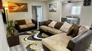 Ein modernes Wohnzimmer mit einem Ecksofa, einem Essbereich mit Tisch und Stühlen und einem Deckenventilator.