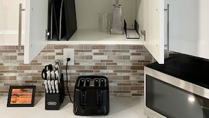 Eine Küche mit weißen Schränken, einer Mikrowelle, einem Toaster und einer Spritzschutzwand mit Ziegeloptik.