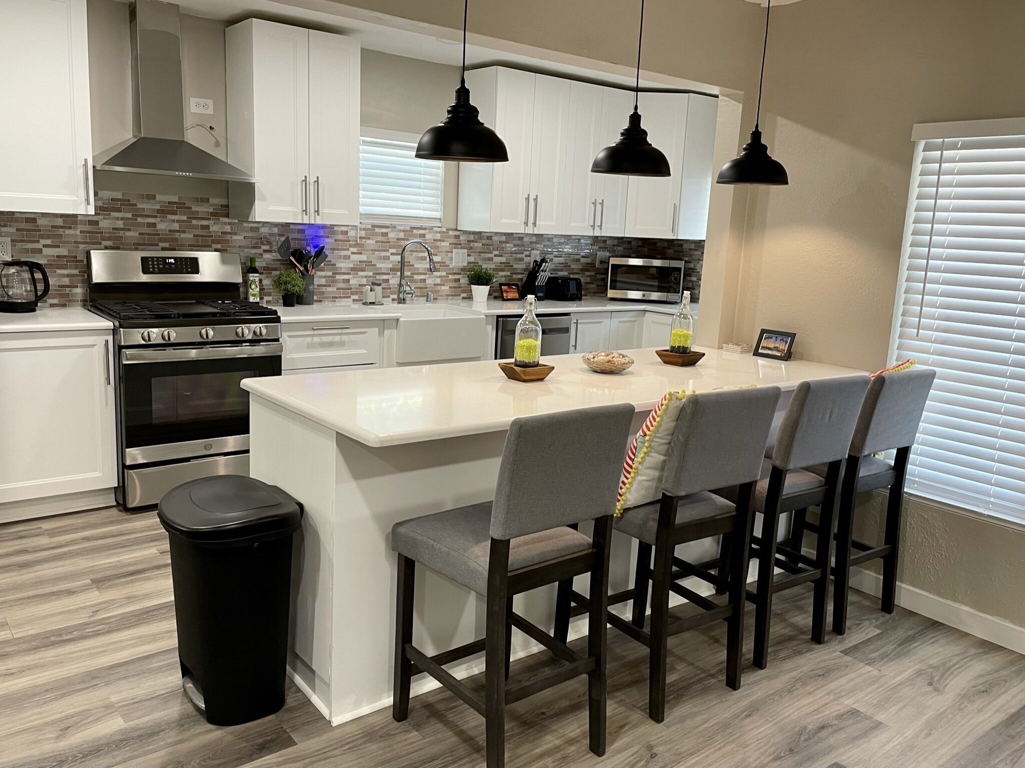 Een moderne keuken met witte kasten, een roestvrijstalen fornuis en een centraal eiland met barkrukken.
