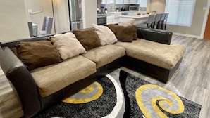 Ein modernes Wohnzimmer mit einer Eckcouch, einer Küche im Hintergrund und einem Essbereich.