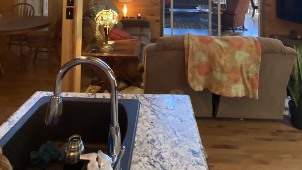 A wooden cabin interior with a kitchen area, dining space, and a living room with a couch and a TV.